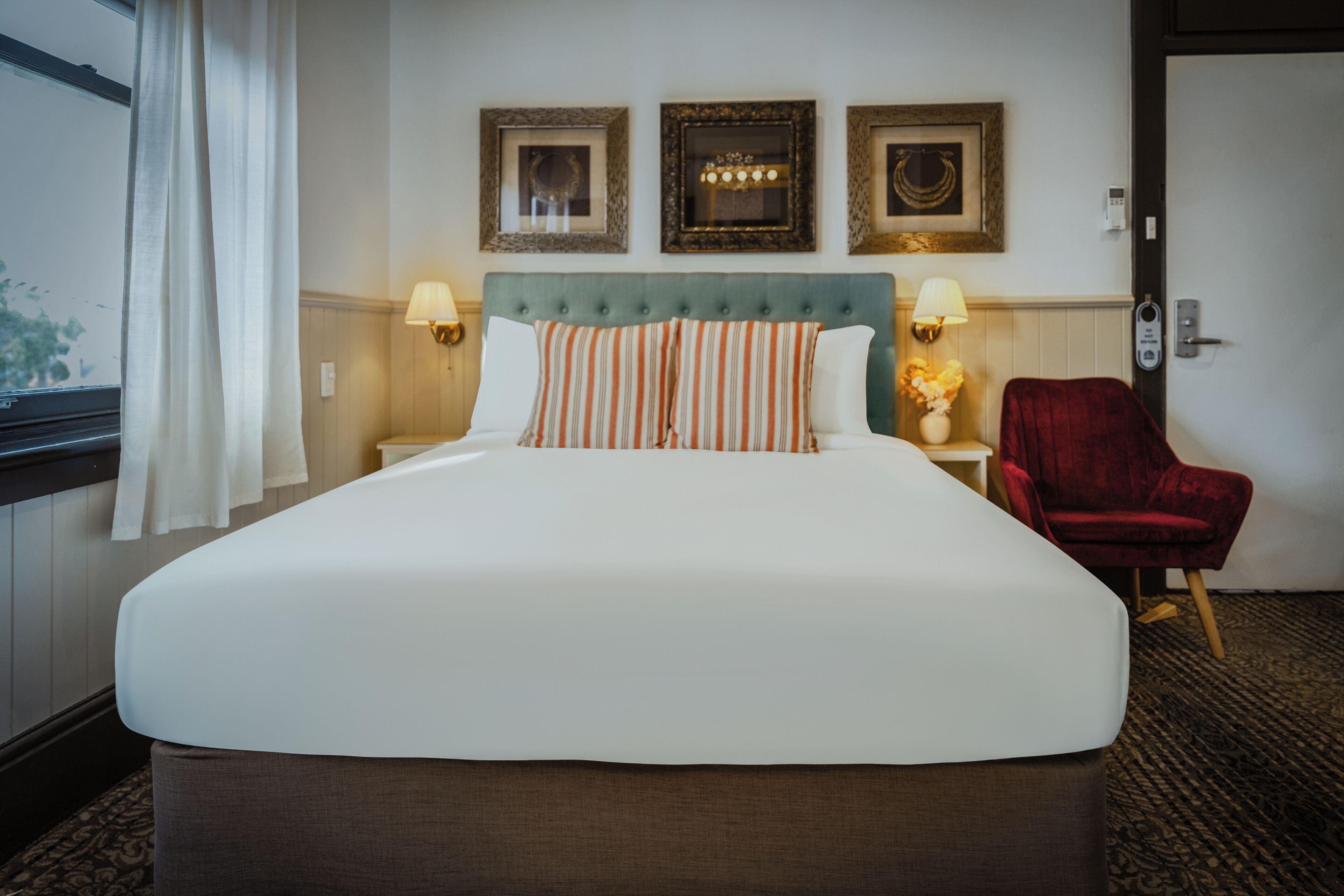 Ein Hotelzimmer mit einem großen Bett, zwei Nachttischlampen, einem roten Sessel und drei gerahmten Bildern an der Wand.