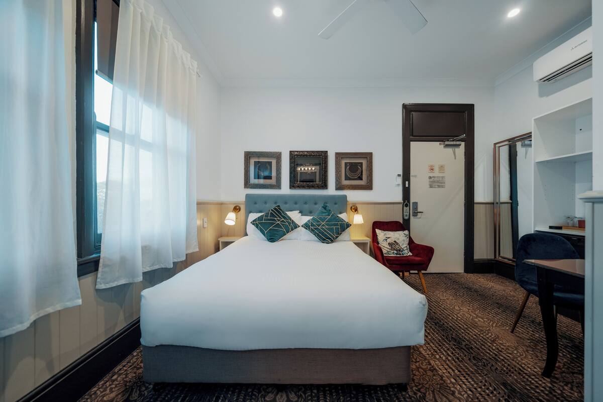 Ein Hotelzimmer mit einem großen Bett, einem roten Sessel, einem Schreibtisch und einer Tür.