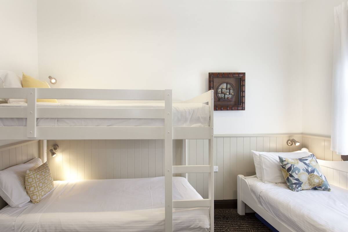 Ein Zimmer mit zwei Etagenbetten, einem kleinen Nachttisch mit Lampe und einem gerahmten Bild an der Wand.
