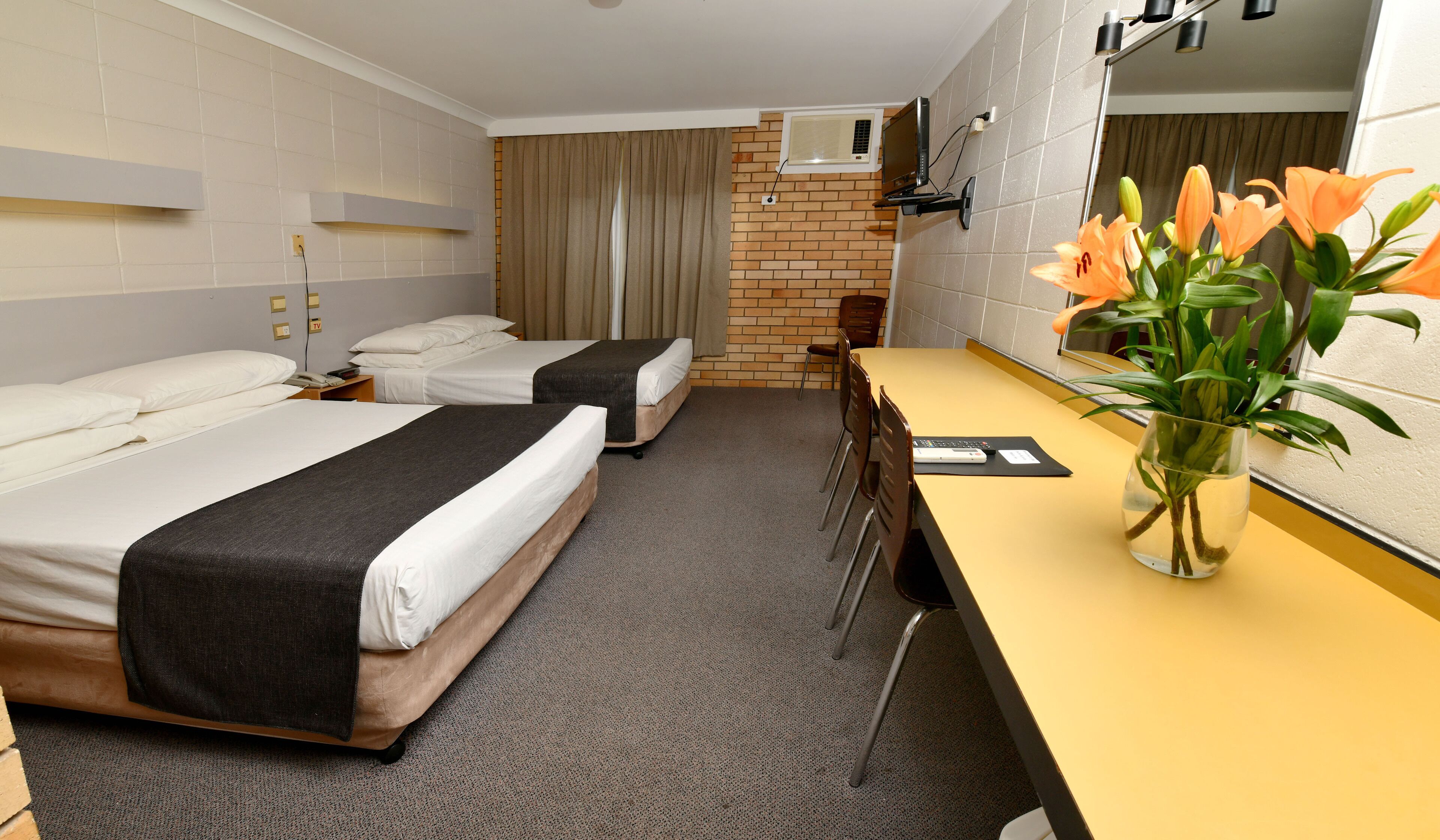 Een hotelkamer met twee bedden, een bureau, een stoel, een televisie en een raam met gordijnen.