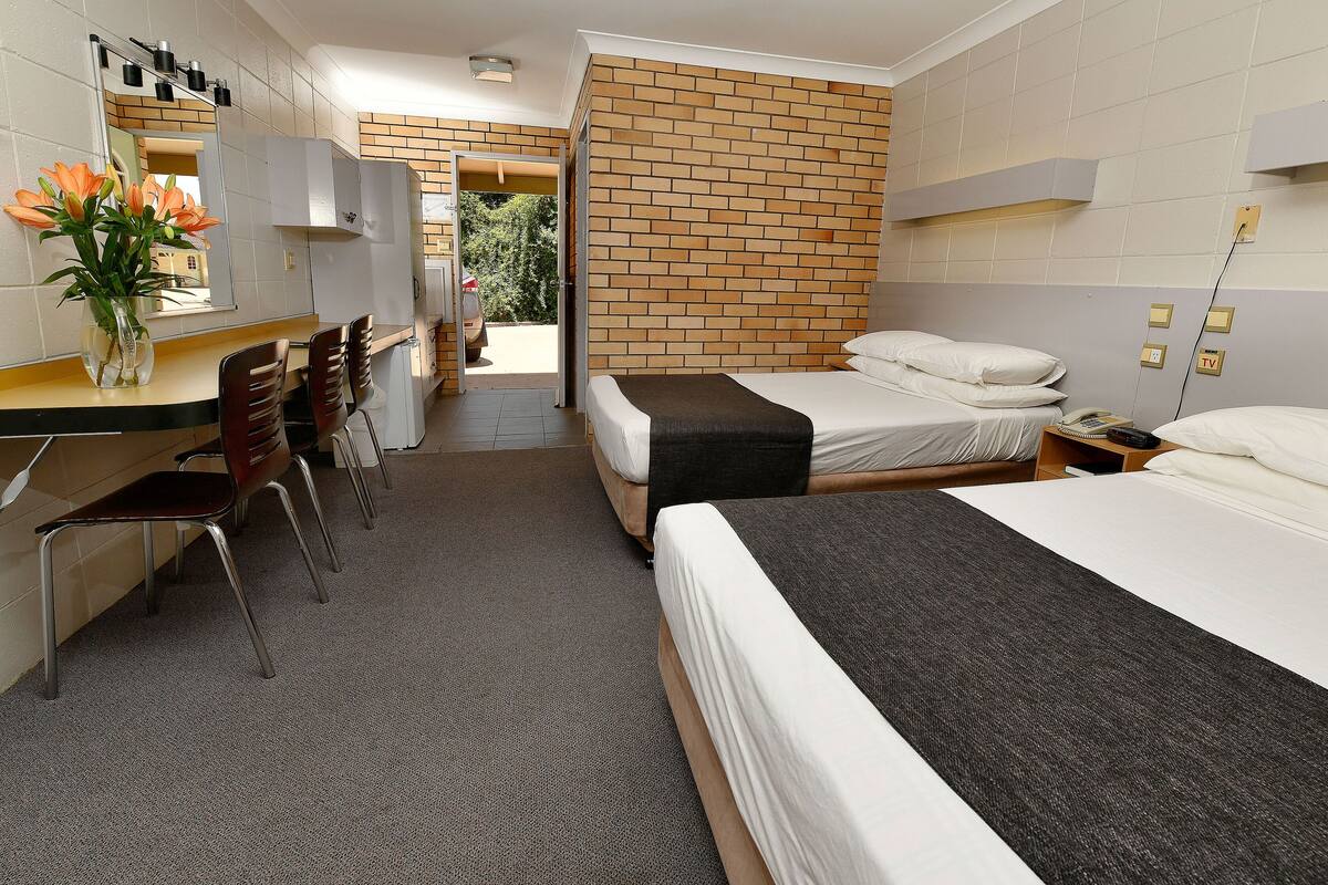 Habitación de hotel con dos camas, un escritorio, sillas, un espejo y una pared de ladrillo.