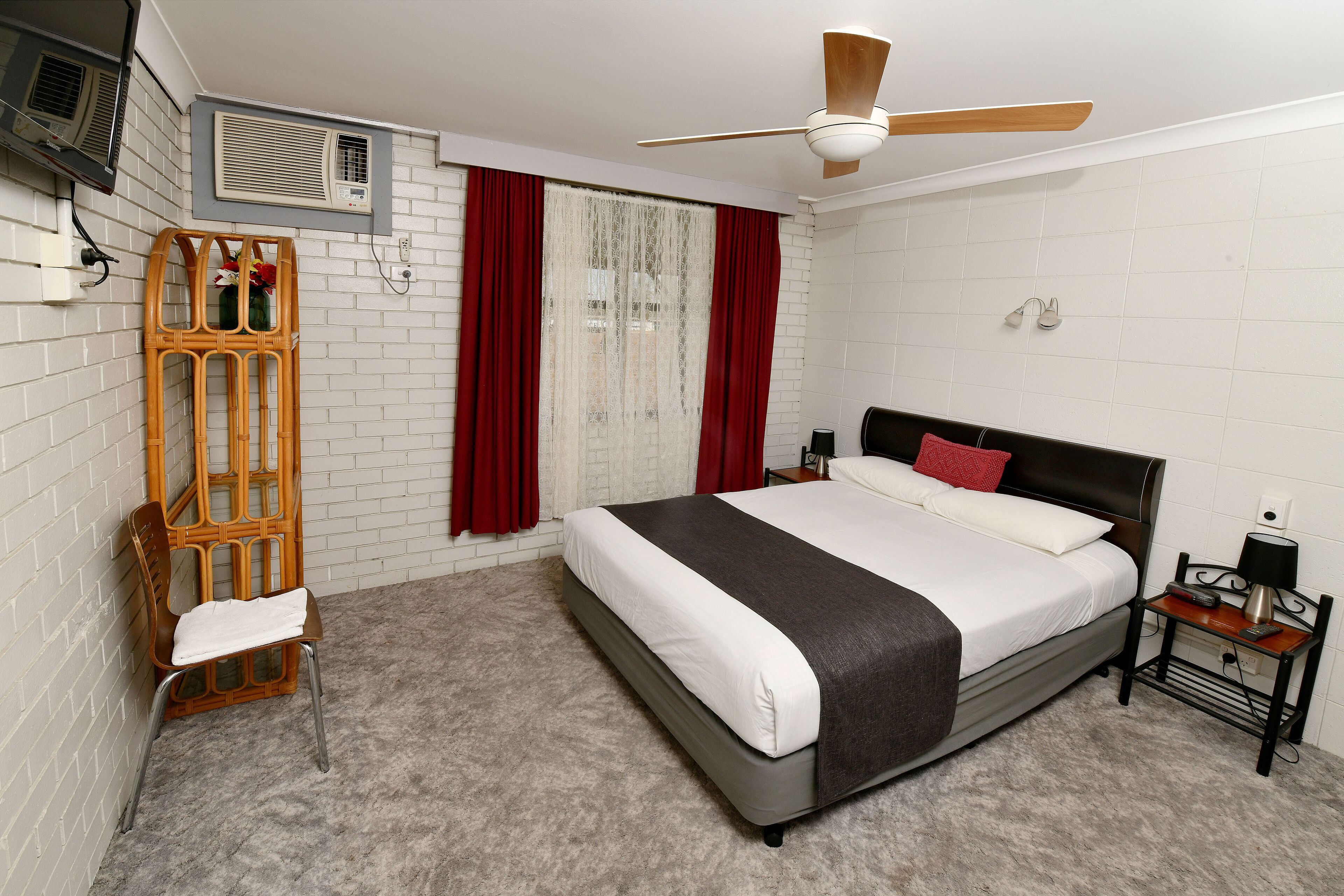 A bedroom with a bed, a nightstand, a chair, a window with curtains, and a ceiling fan.