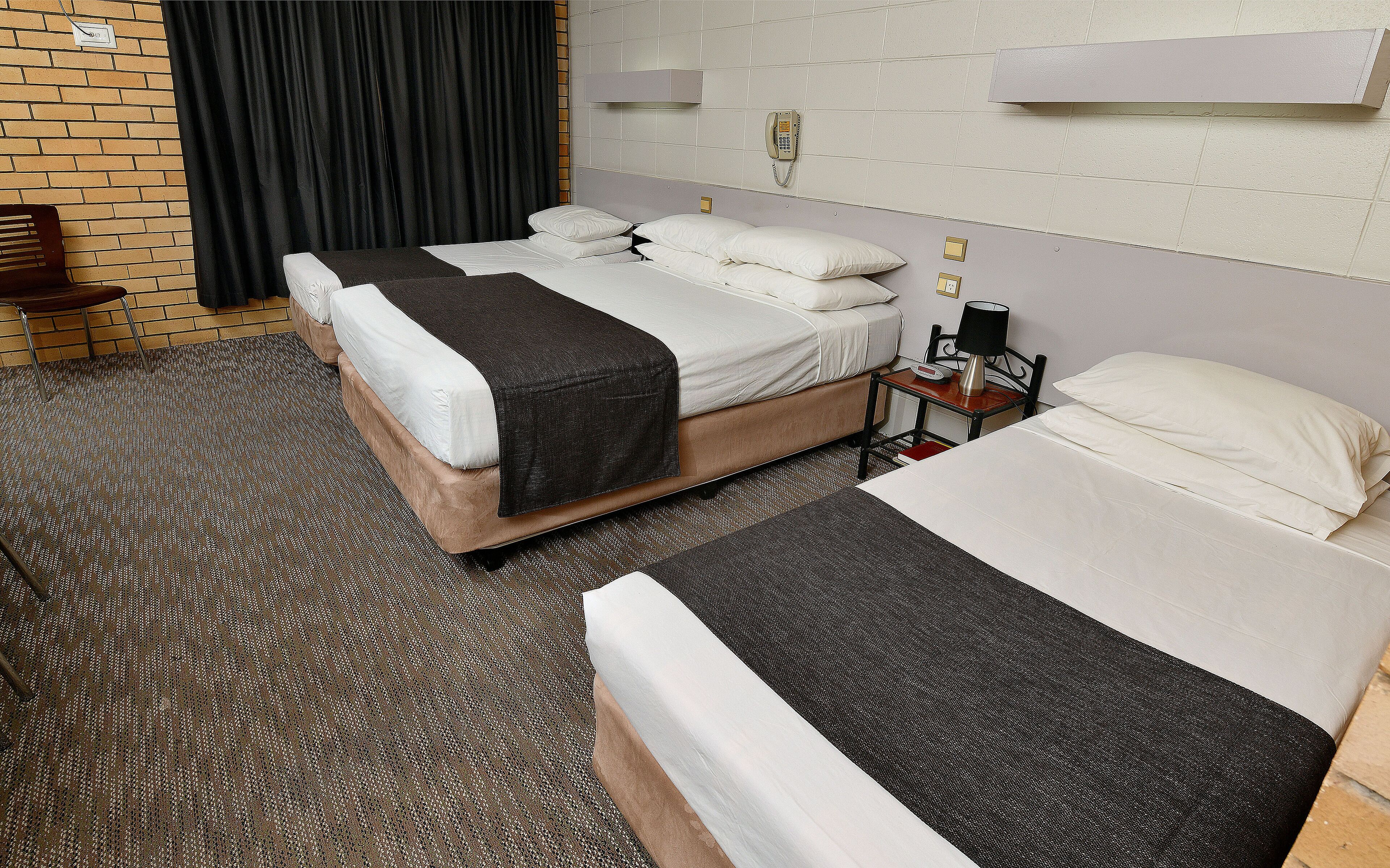A hotel room with two beds, a telephone, a desk with a lamp, and a brick wall.