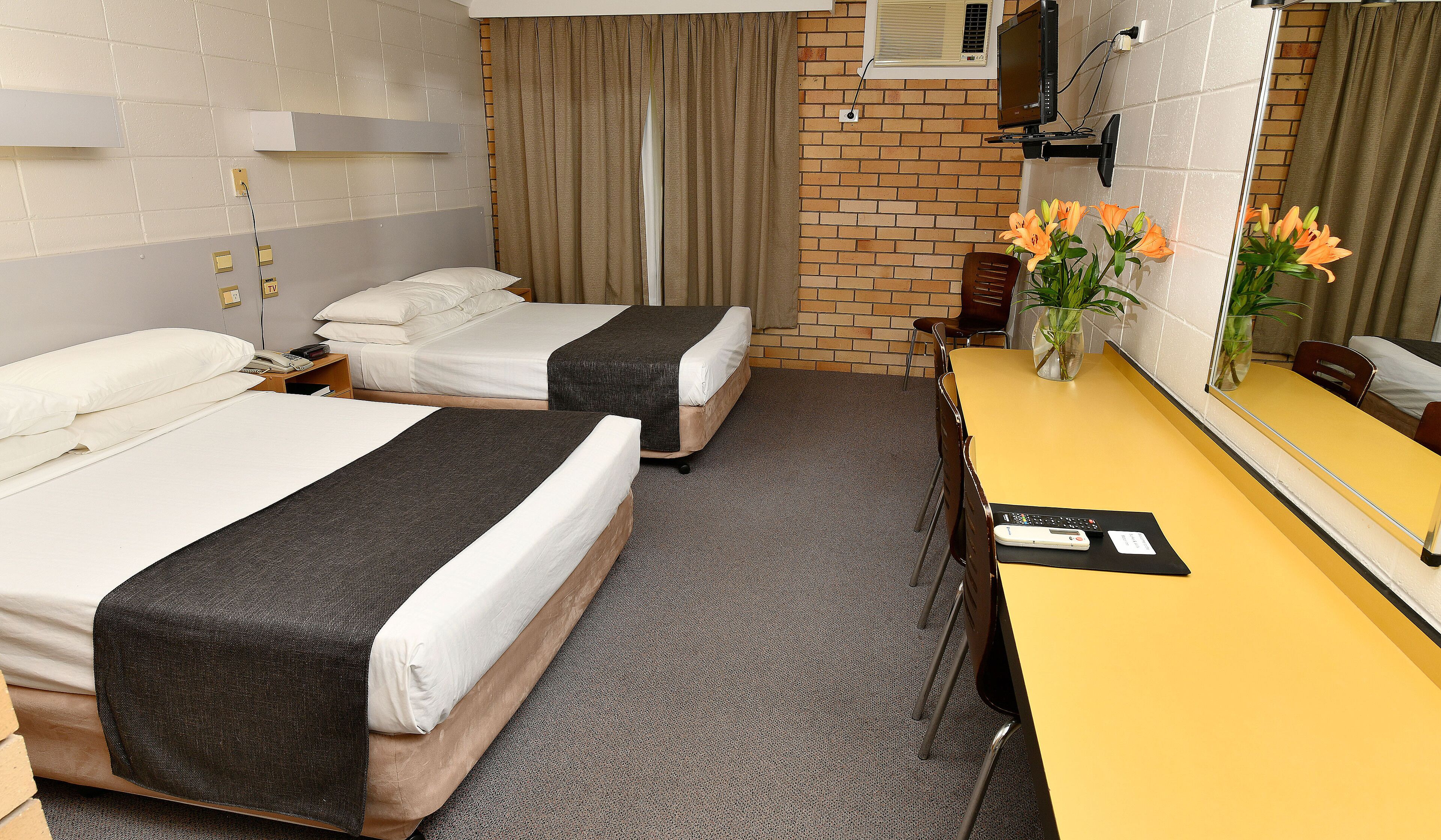 A hotel room with two beds, a desk, a chair, a mirror, and a vase with flowers.