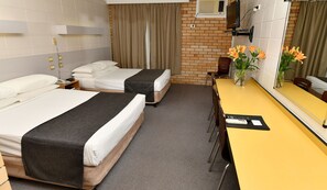A hotel room with two beds, a desk, a chair, a mirror, and a vase with flowers.