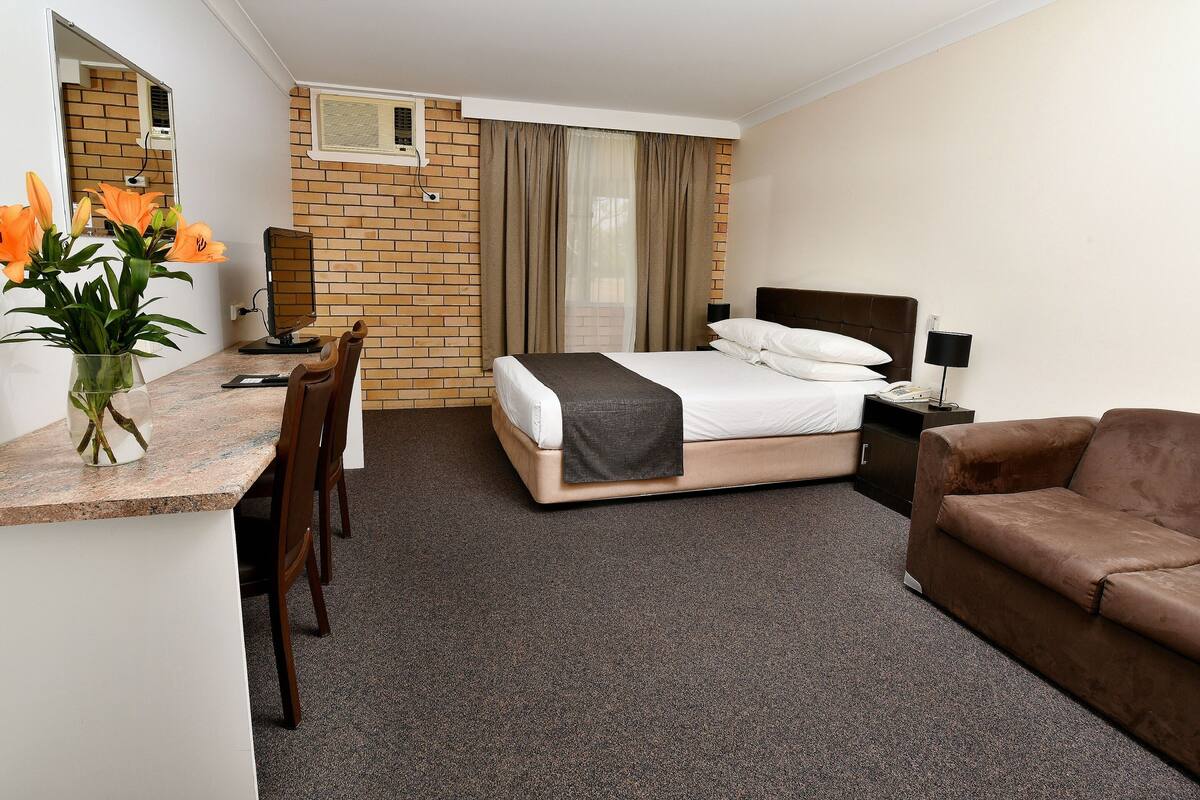 Una habitación de hotel con cama, escritorio, silla, sofá y espejo.