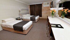 A hotel room with two beds, a desk, a chair, a telephone, a TV, and a vase with flowers.
