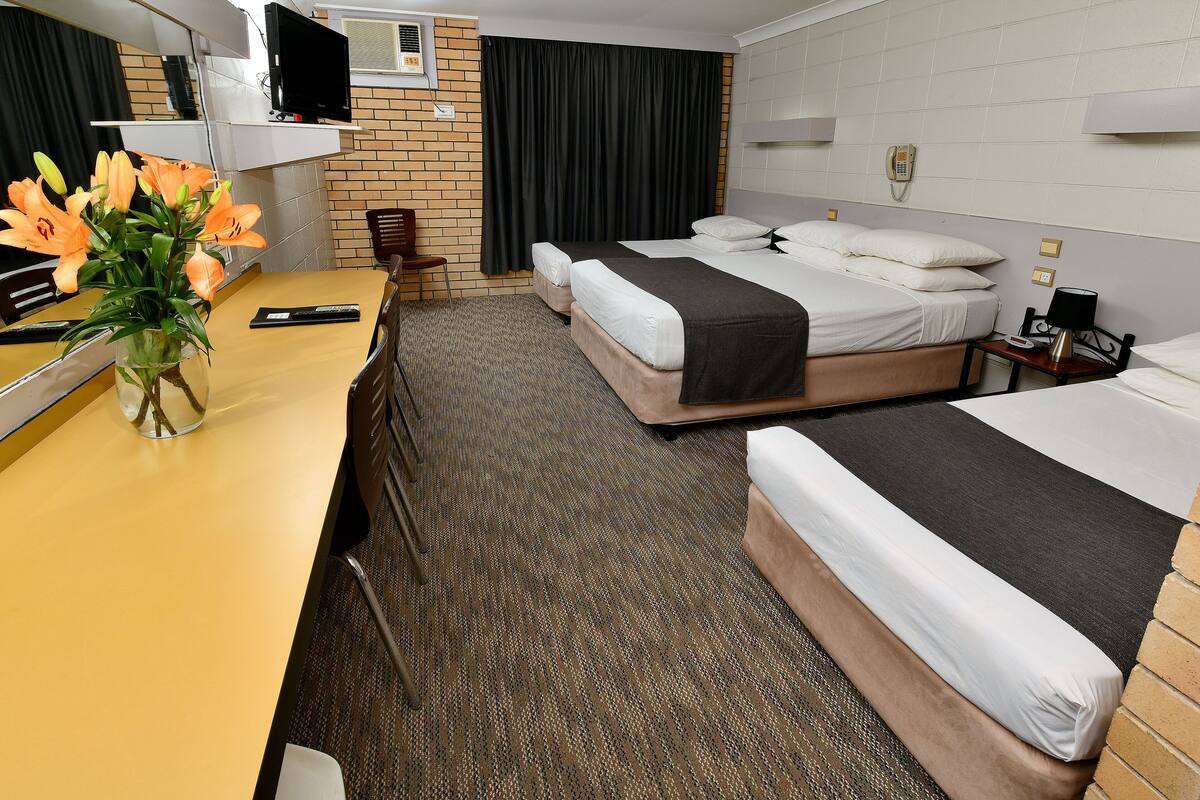 Una habitación de hotel con dos camas, un escritorio, una silla, un jarrón con flores, un televisor y un teléfono.