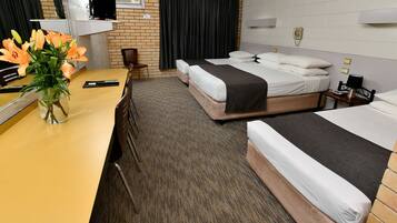 A hotel room with two beds, a desk, a chair, a vase with flowers, a television, and a telephone.