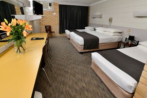 A hotel room with two beds, a desk, a chair, a vase with flowers, a television, and a telephone.
