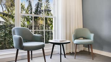 Dos sillones y una mesita baja en una habitación con un ventanal grande con vistas a un jardín.