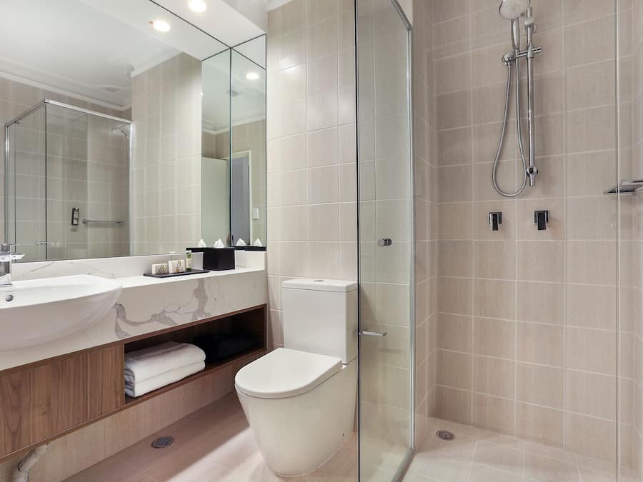 Un baño moderno con ducha envuelta en vidrio, un espejo grande y un tocador con dos lavabos.