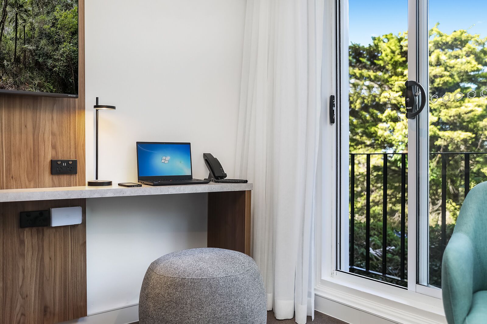 Una habitación moderna con escritorio, computadora portátil, teléfono y reposapiés.