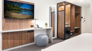 A modern bedroom with a TV mounted on the wall, a desk with a phone, a small plant, and a wardrobe with a mirror. - Killara Hotel & Suites (Killara)