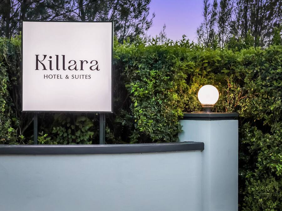 Letrero del Hotel & Suites Killara, con un seto bien cuidado y una lámpara esférica.