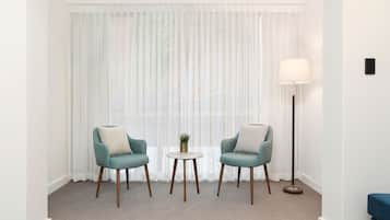 A hotel room with two teal armchairs, a small round table with a plant, and a floor lamp.