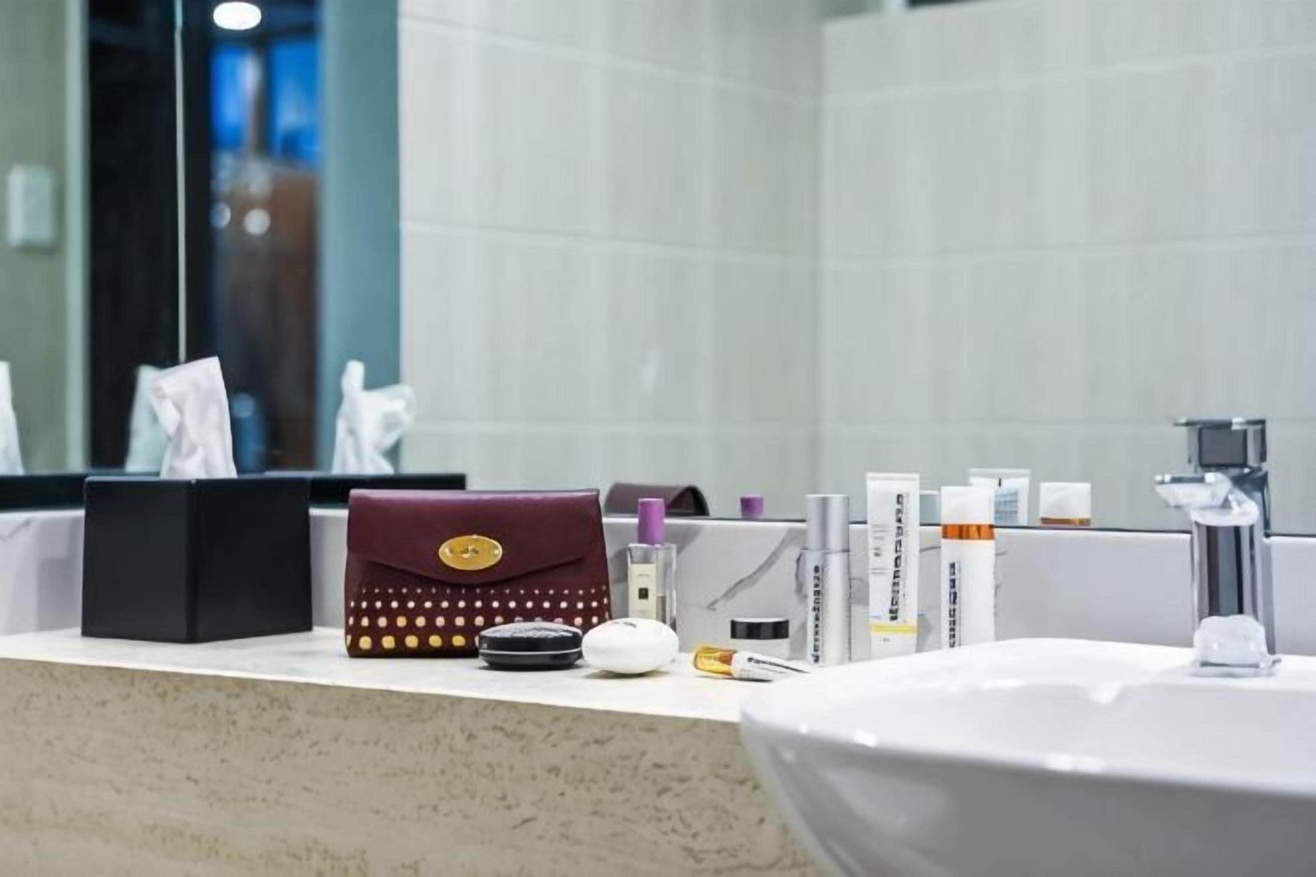 A bathroom counter with toiletries, a mirror, and a sink.
