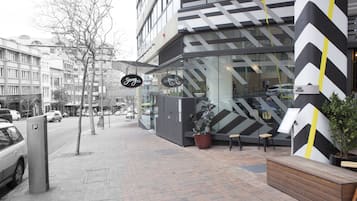 A modern building with a glass facade, a black and white chevron pattern on the exterior, and a wooden bench outside.