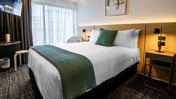 Une chambre d’hôtel avec un grand lit, un téléviseur fixé au mur, un bureau avec une chaise et une fenêtre avec des rideaux.