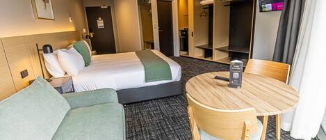 A hotel room with a bed, a sofa, a dining table, and a TV.