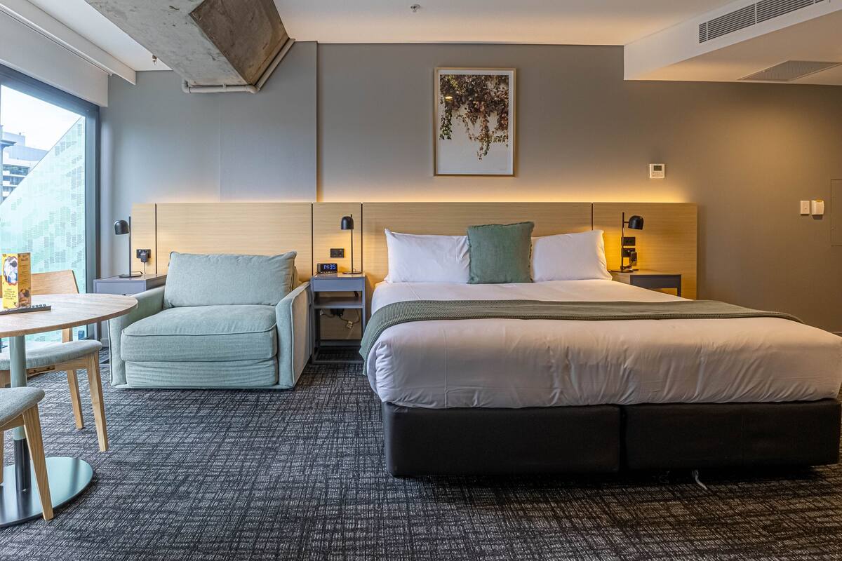 Habitación de hotel moderna con una cama grande, un pequeño sofá, una mesa redonda y vistas a un edificio.