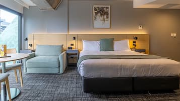 Habitación de hotel moderna con una cama grande, un pequeño sofá, una mesa redonda y vistas a un edificio.