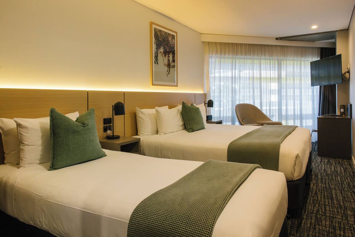 Habitación de hotel con dos camas, un escritorio, una silla, un televisor y una ventana con cortinas.
