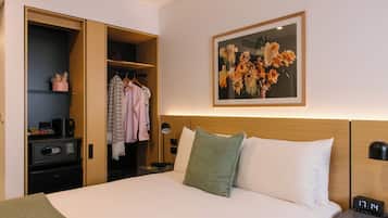 A hotel room with a bed, a nightstand, a desk, a wardrobe, and a framed floral artwork on the wall.