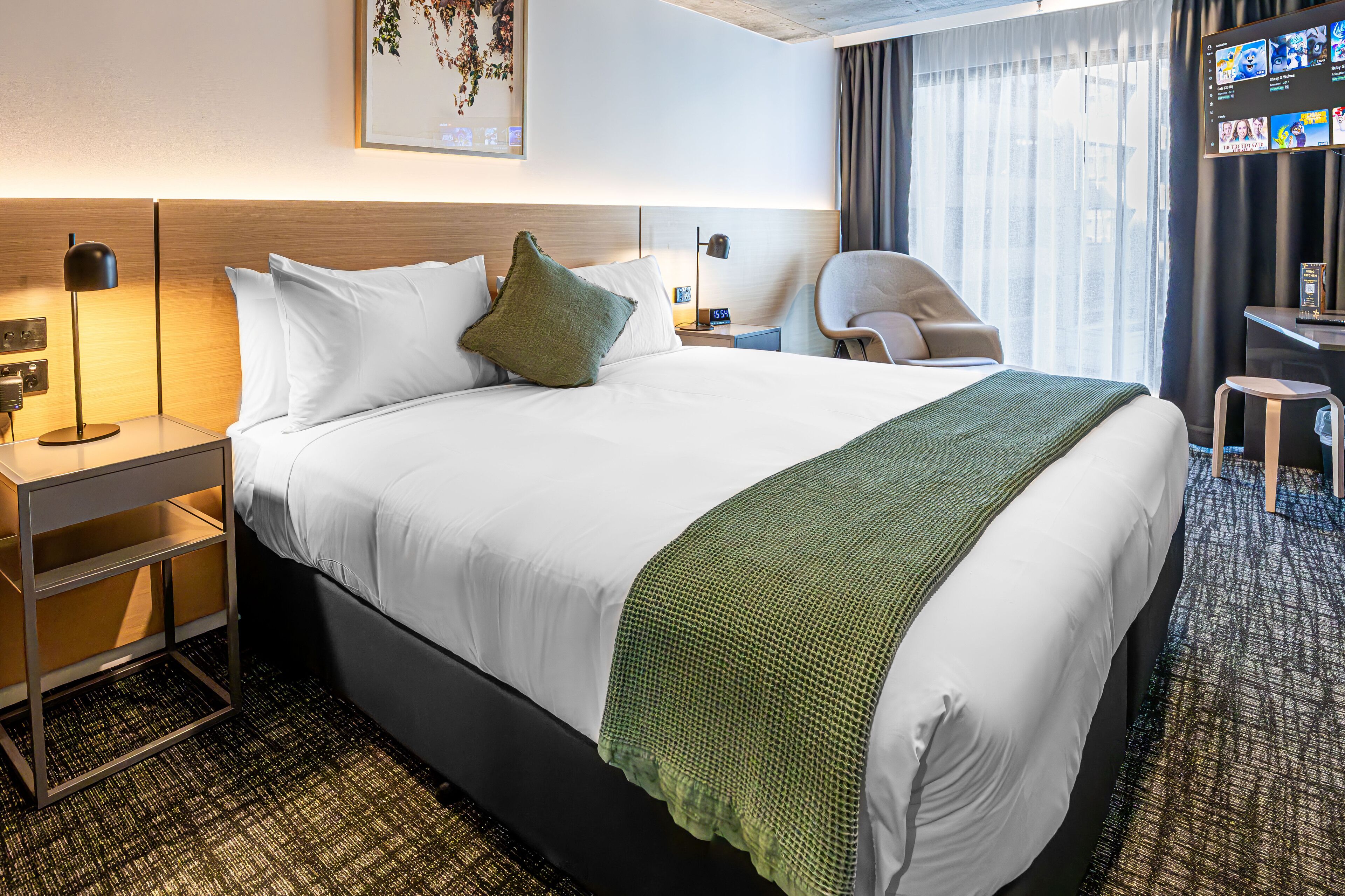 A hotel room with a bed, a desk, a chair, a TV, and a window with curtains.