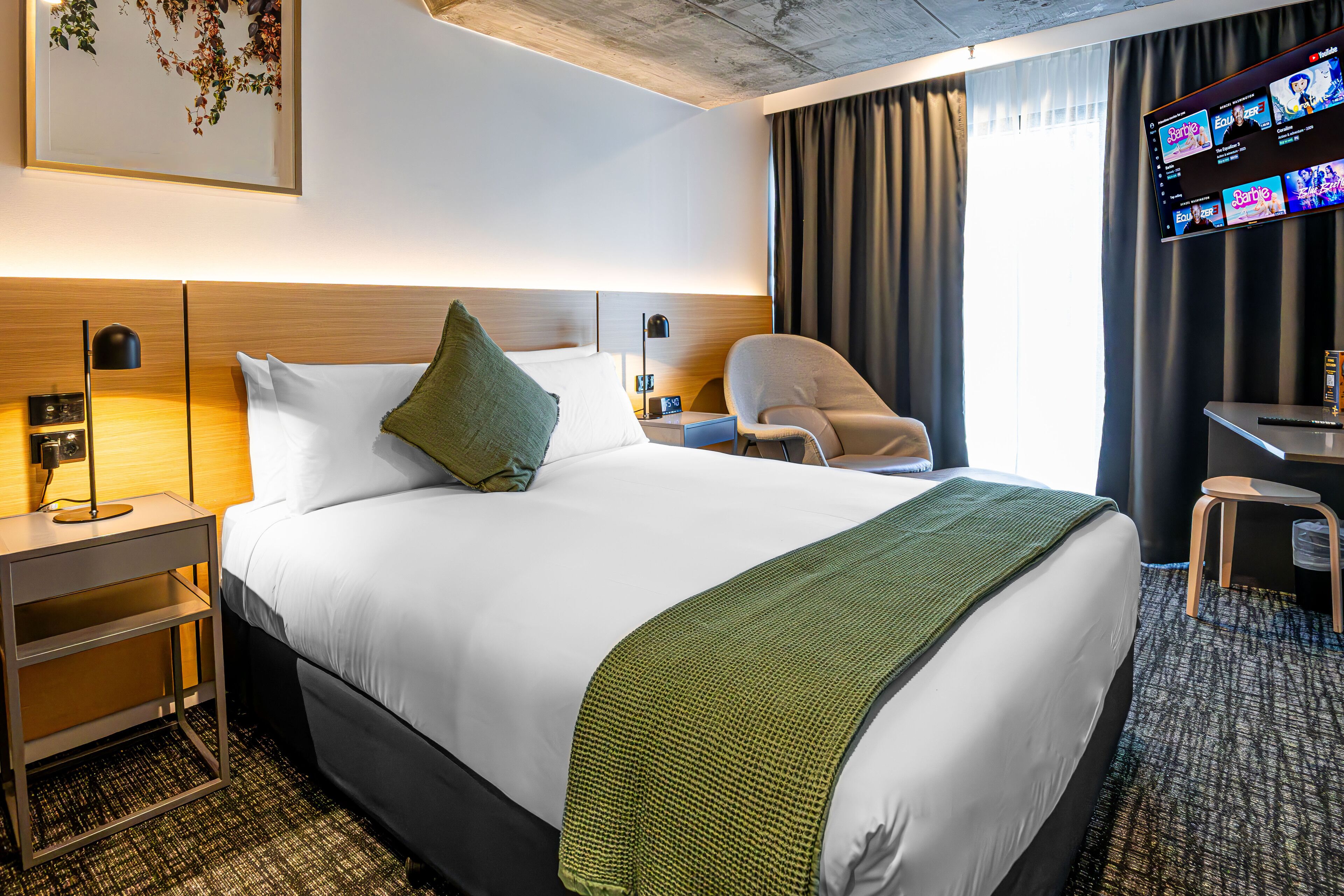 Una habitación de hotel con una cama grande, un escritorio, una silla, un televisor y una obra de arte colgada en la pared.