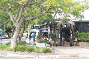 A cafe with outdoor seating, a signboard, and a tree in the foreground. - Hamilton Motor Inn (Hamilton)