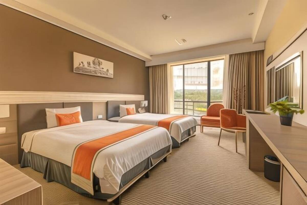 A hotel room with two beds, a desk, a chair, and a large window with curtains.
