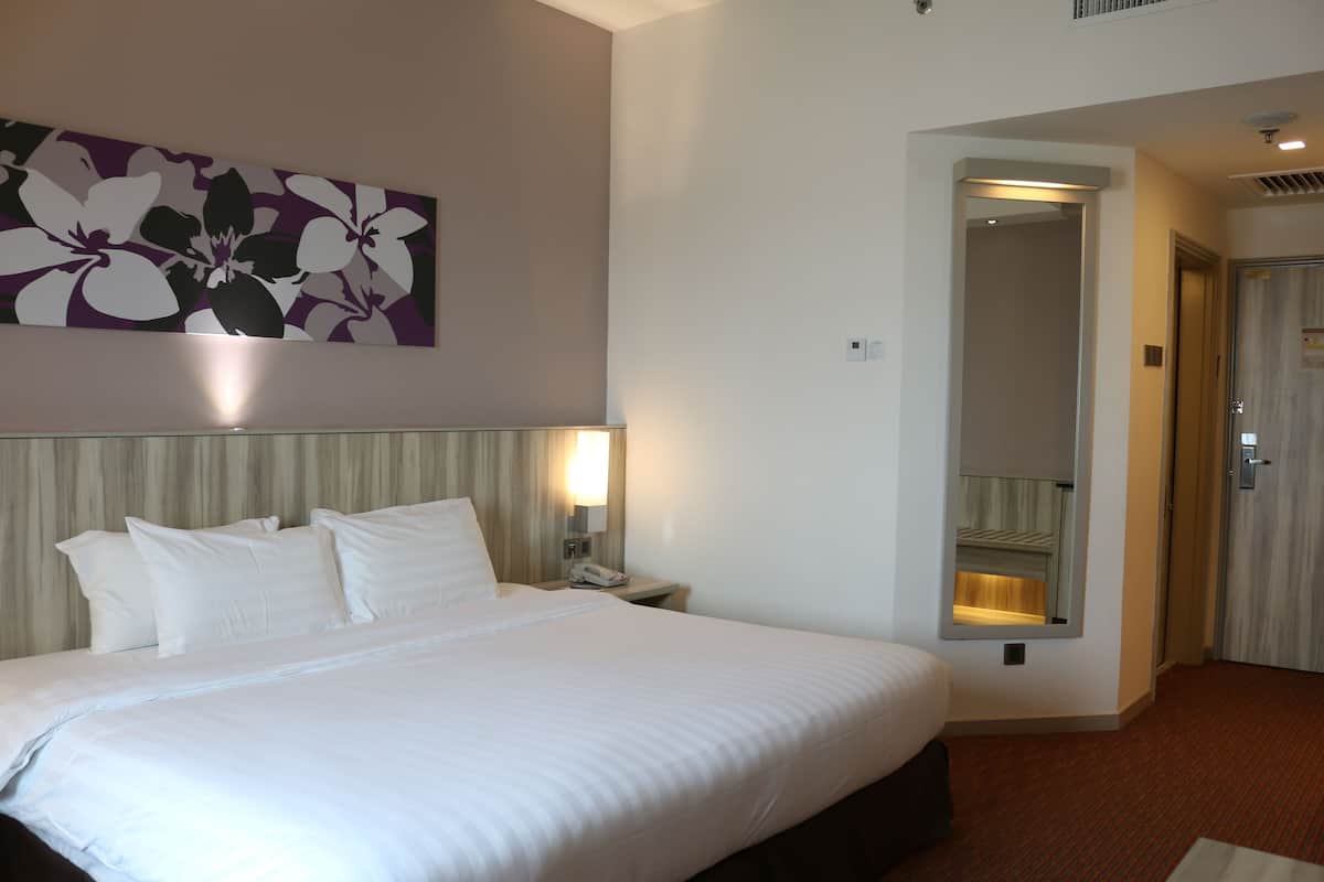 A hotel room with a large bed, a nightstand with a lamp, a mirror, and a door leading to another room.