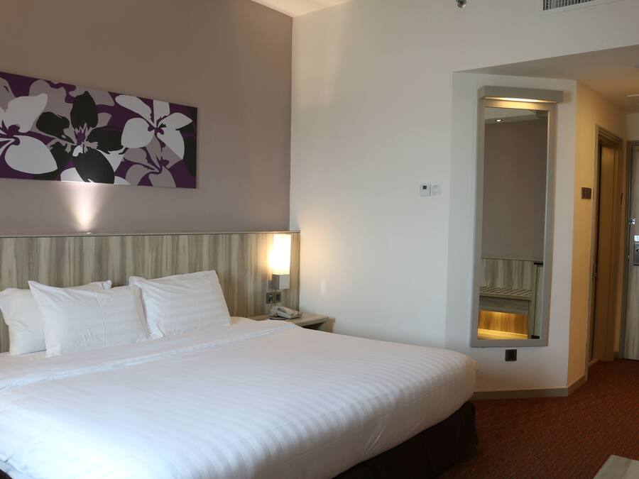A hotel room with a large bed, a nightstand with a lamp, a mirror, and a door leading to another room.