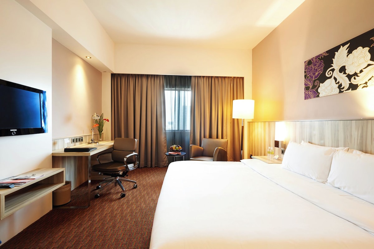 A hotel room with a bed, desk, chair, television, and a window with curtains.