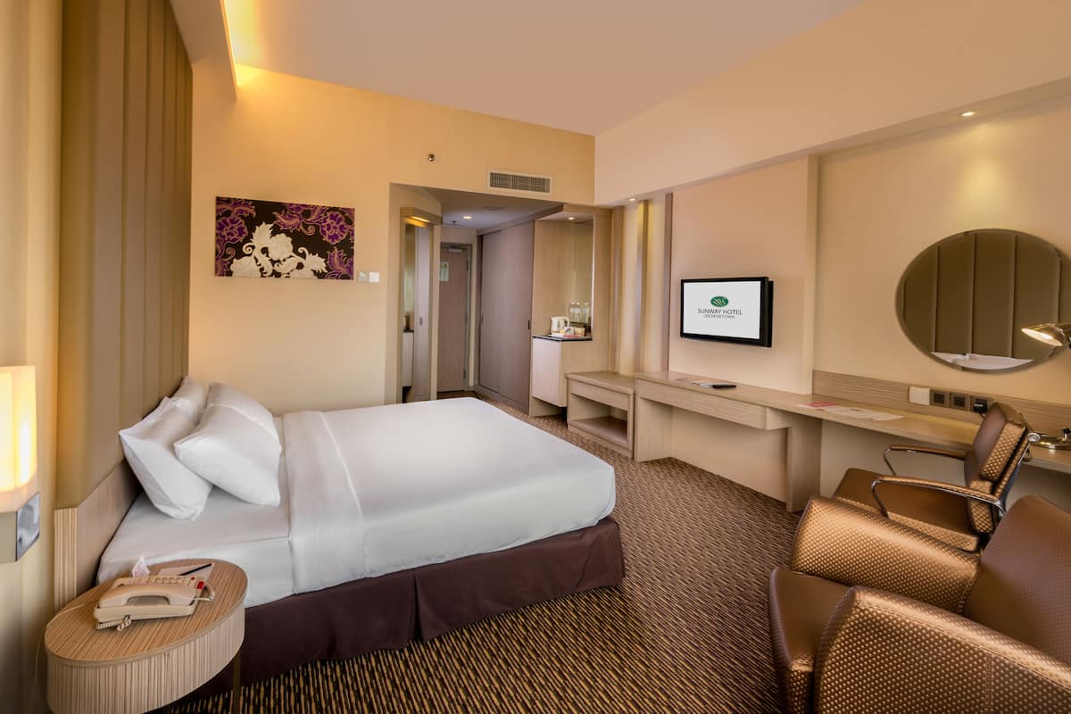 Quarto de hotel com cama, escrivaninha, cadeira, televisão e banheiro.