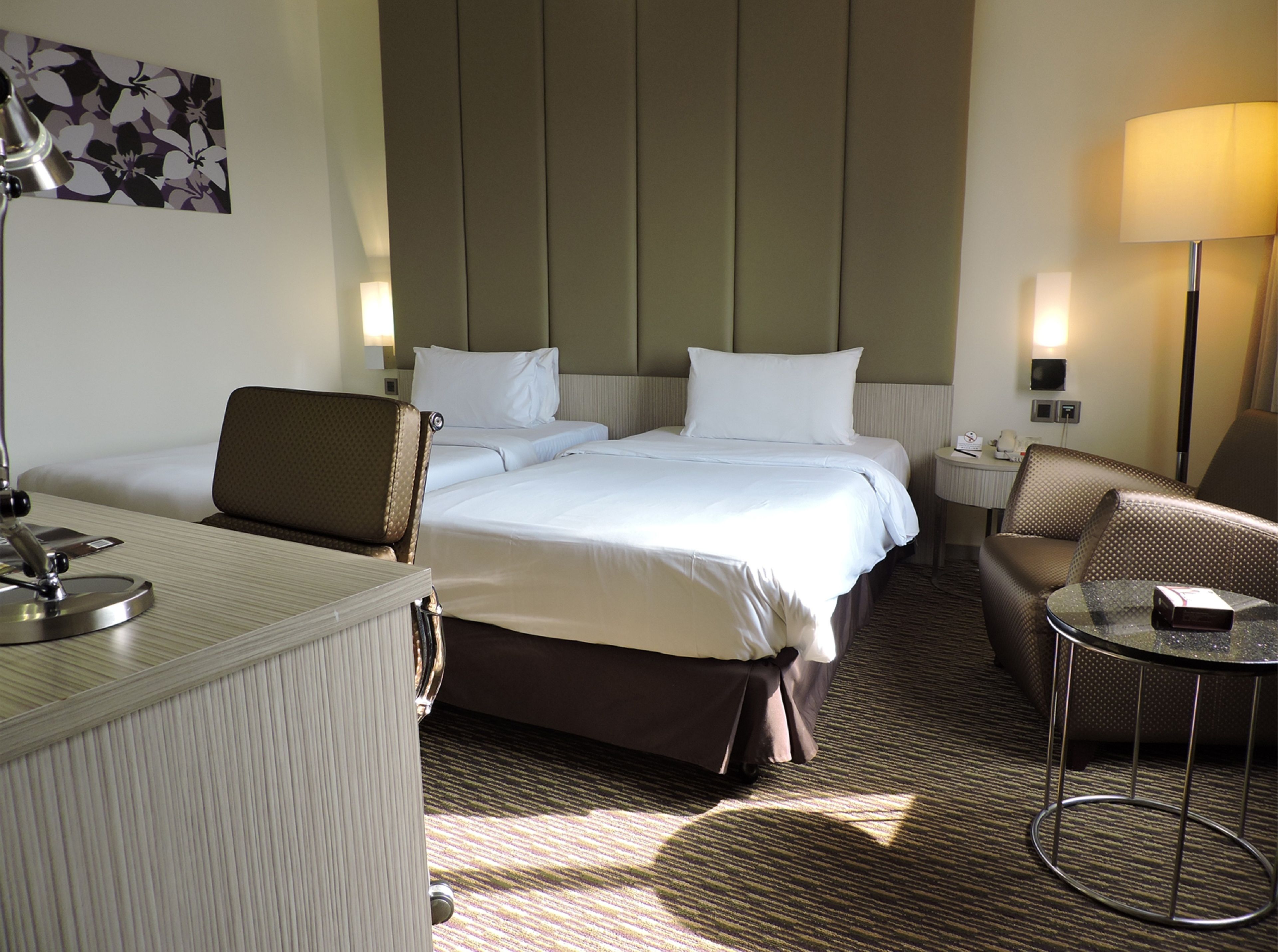 Une chambre d’hôtel avec un lit, deux chaises, un bureau et une lampe.