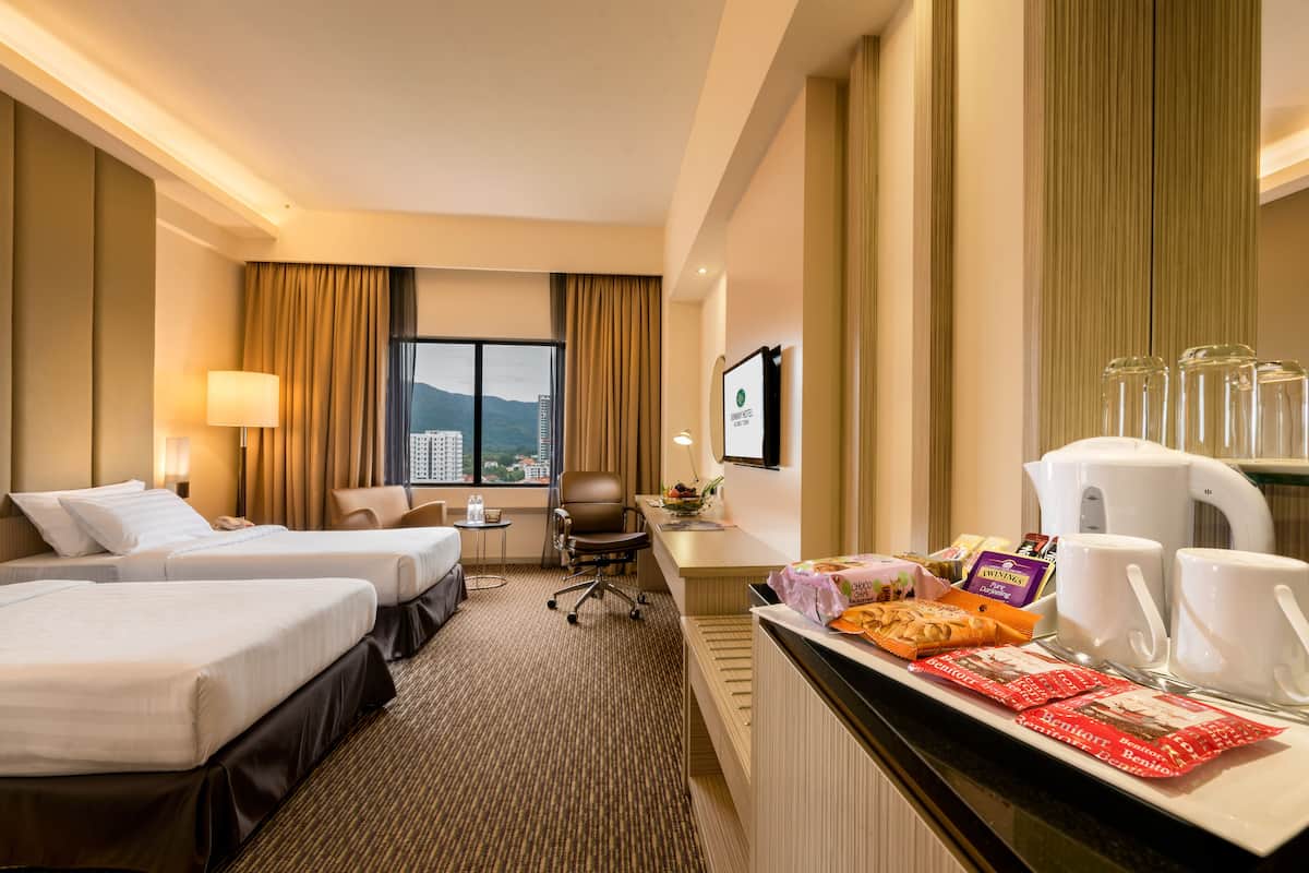 Quarto de hotel com duas camas, uma mesa com chávenas de café e snacks, uma cadeira e vista para a cidade.