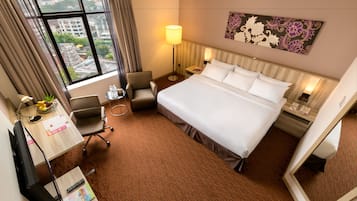Una camera d'albergo con un letto grande, una scrivania con un computer, una sedia, una lampada e vista sulla città dalla finestra.