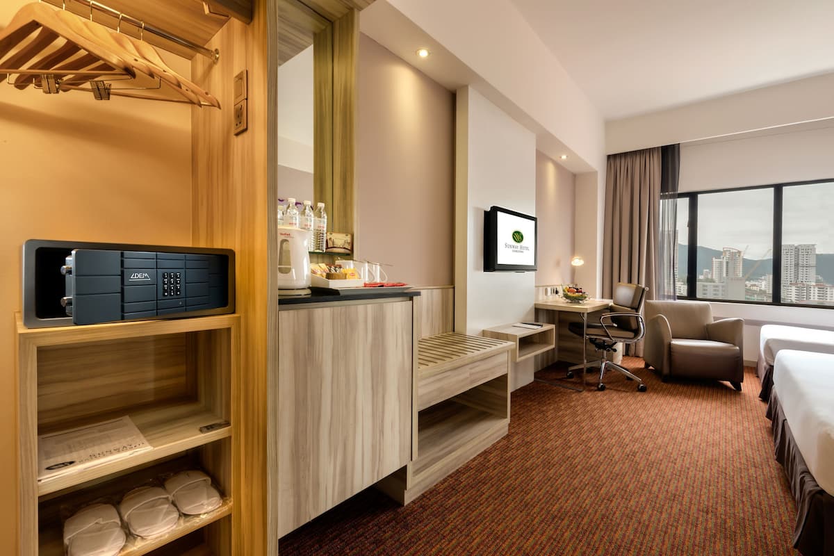 Quarto de hotel com secretária de madeira, uma cadeira, cama, televisão e vista para a cidade.