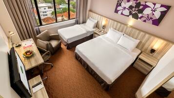 A hotel room with two beds, a desk with a computer, a chair, and a window with a city view.