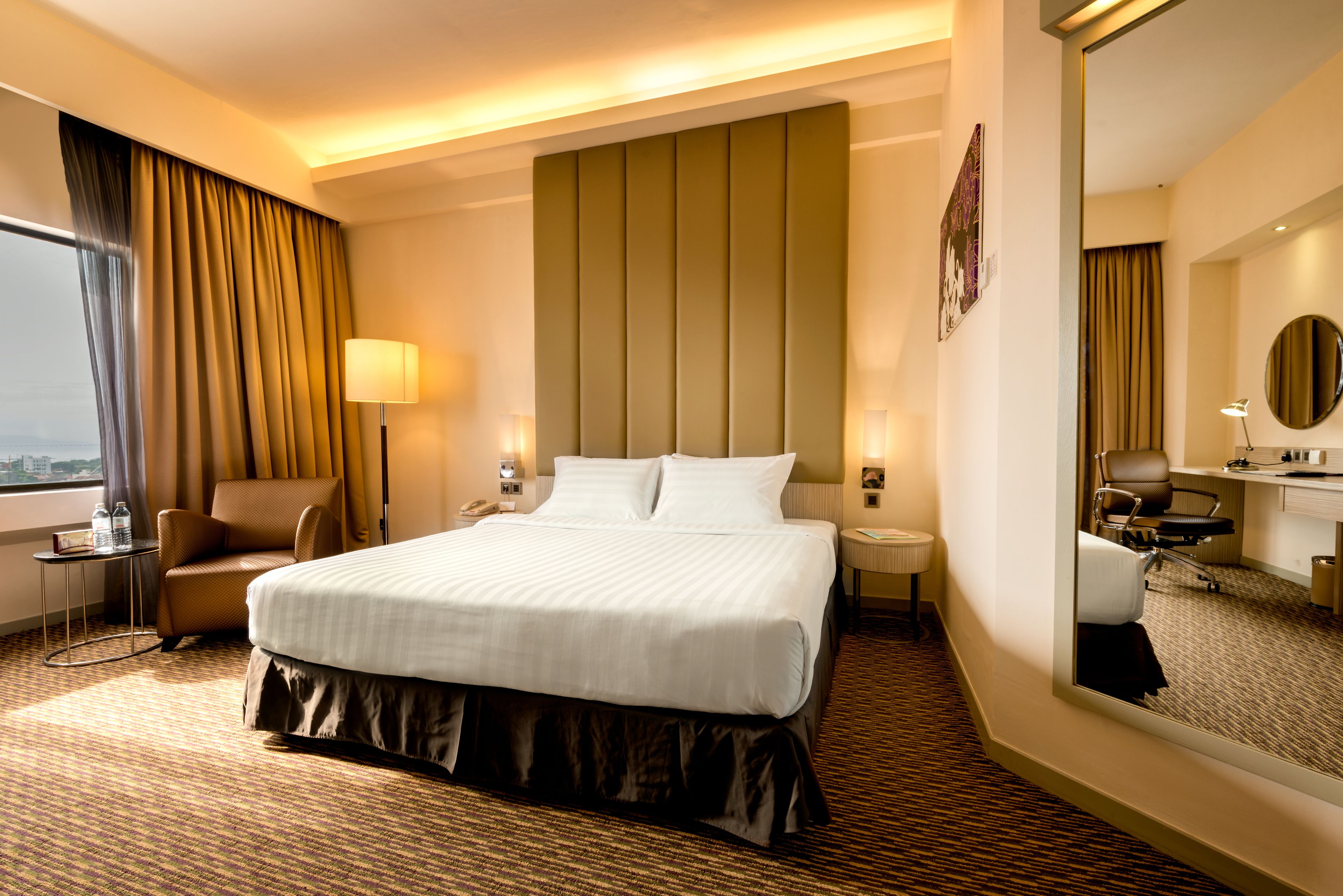 A hotel room with a large bed, a chair, a desk, and a mirror.