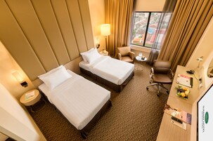 Habitación de hotel con dos camas, un escritorio con computadora, una silla, una lámpara y una ventana con cortinas.