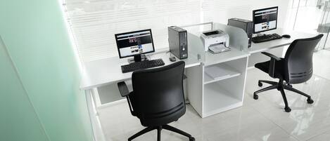 A modern office with two desks, each with a computer, keyboard, and mouse. There are two office chairs and a printer on the desks.