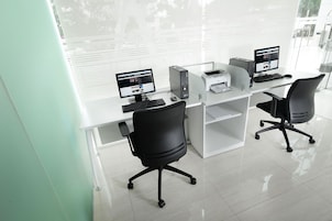 A modern office with two desks, each with a computer, keyboard, and mouse. There are two office chairs and a printer on the desks.