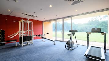 Un gimnasio con equipo de ejercicio, cinta de correr y un amplio ventanal con vistas a zonas verdes.