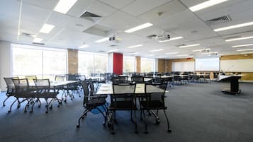 A conference room with multiple tables and chairs, large windows, and a projector screen.