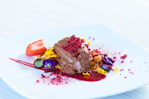 Un plato de postre con un dulce de chocolate, fresas y flores comestibles de colores.