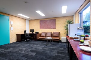 Ein moderner Arbeitsraum mit Backsteinwand, einer braunen Ledersofa, einem Schreibtisch mit Computer und einem Fenster mit Blick auf Grünflächen.