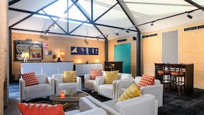 A spacious indoor seating area with white sofas and chairs, a glass coffee table, and a brick wall backdrop. - Lakeside Hotel and Conference Centre (Macquarie Park)